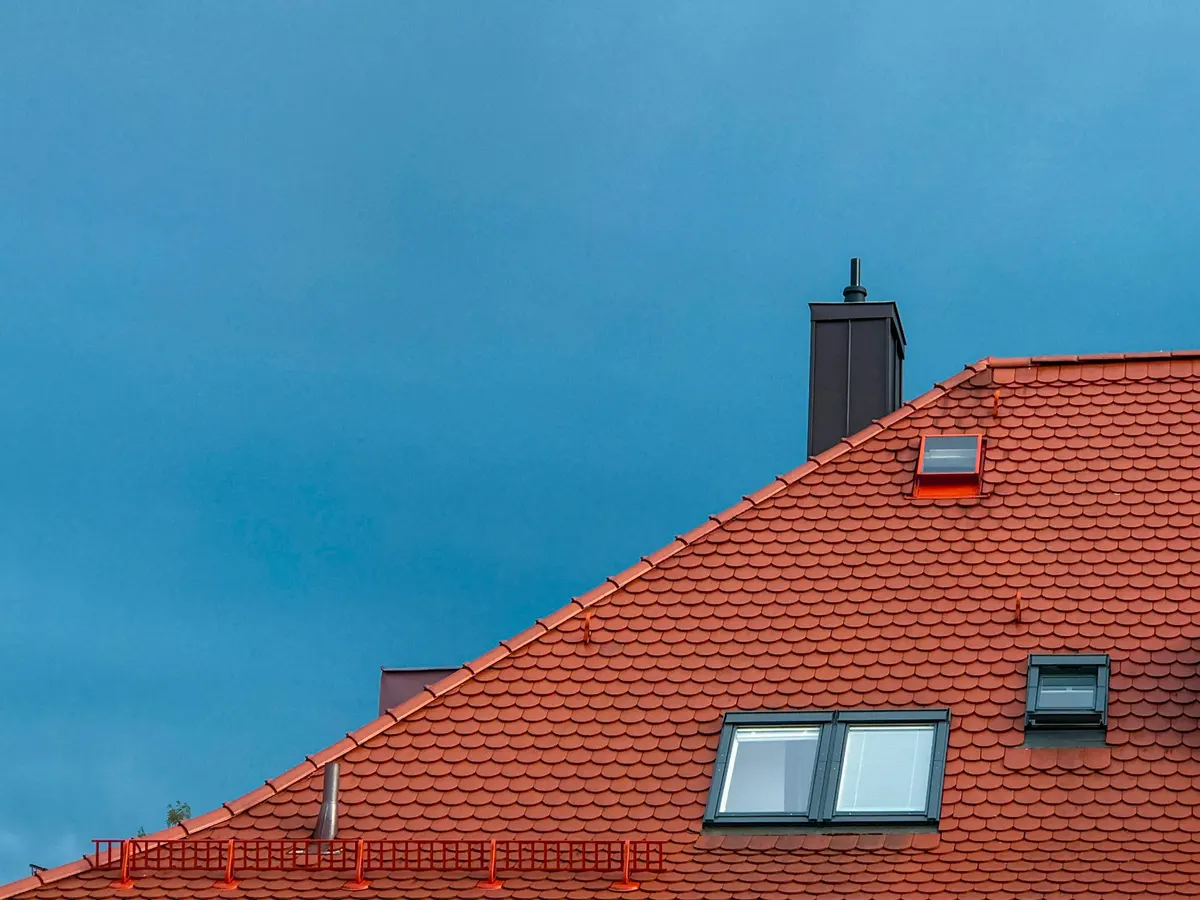 Ziegeldach mit eingebautem Dachfenster und Schornstein vor blauem Himmel