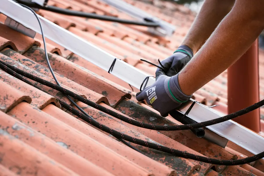 Hände montieren eine Aluminiumschiene für eine Solaranlage auf dem Ziegeldach